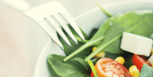 Ensalada saludable con verduras frescas, tomate, espinaca y queso en un plato blanco.